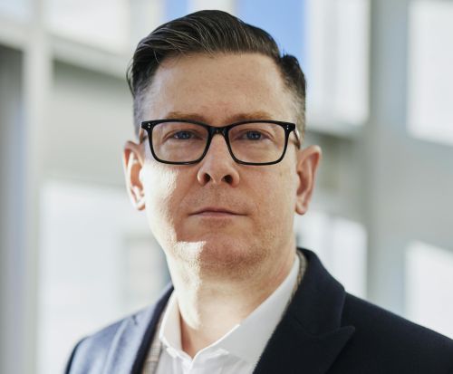 Profile portrait of a confident business executive wearing eyeglasses in a sunlit office setting.
